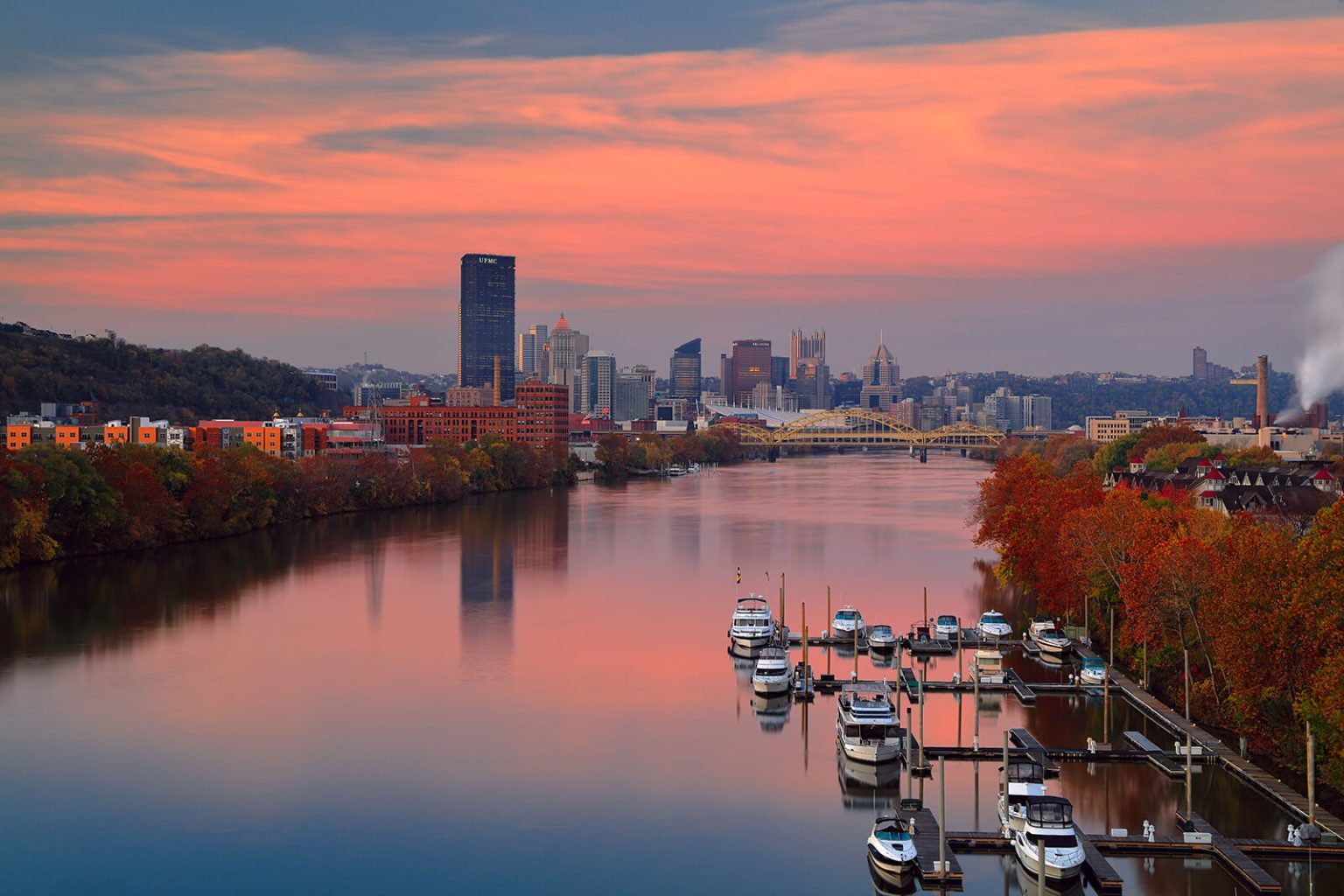 The Allegheny river with boats in it and a city of Pittsburgh in the background during fall